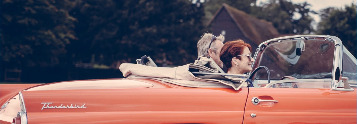 Older Couple driving in red convertible