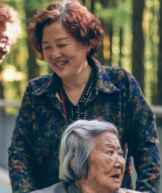 Two Asian Elderly ladies one pushing other in wheel chair